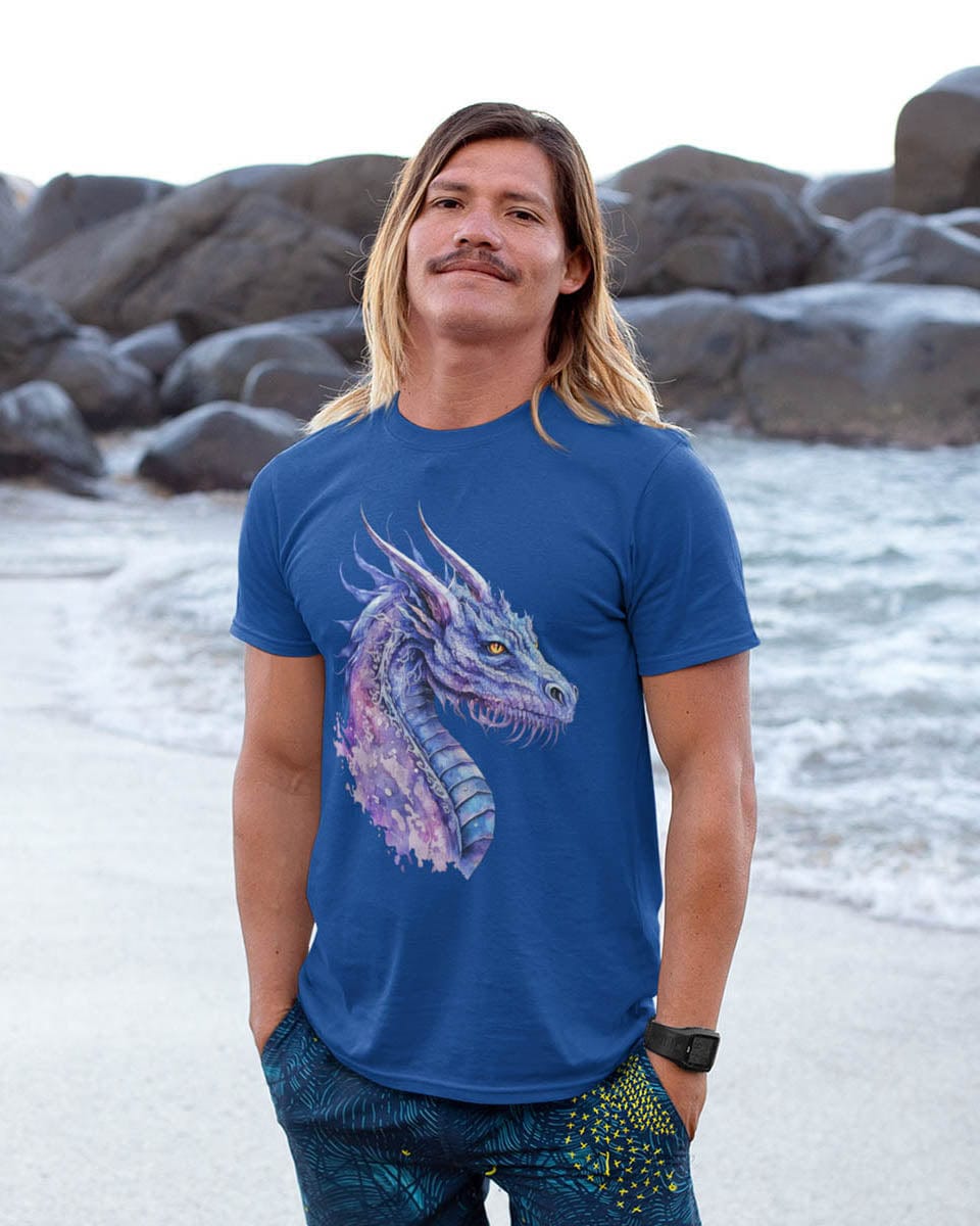 Man standing on a rocky beach wearing an Amethyst Nebula Dragon shirt featuring ethereal watercolor art of an aquatic dragon.