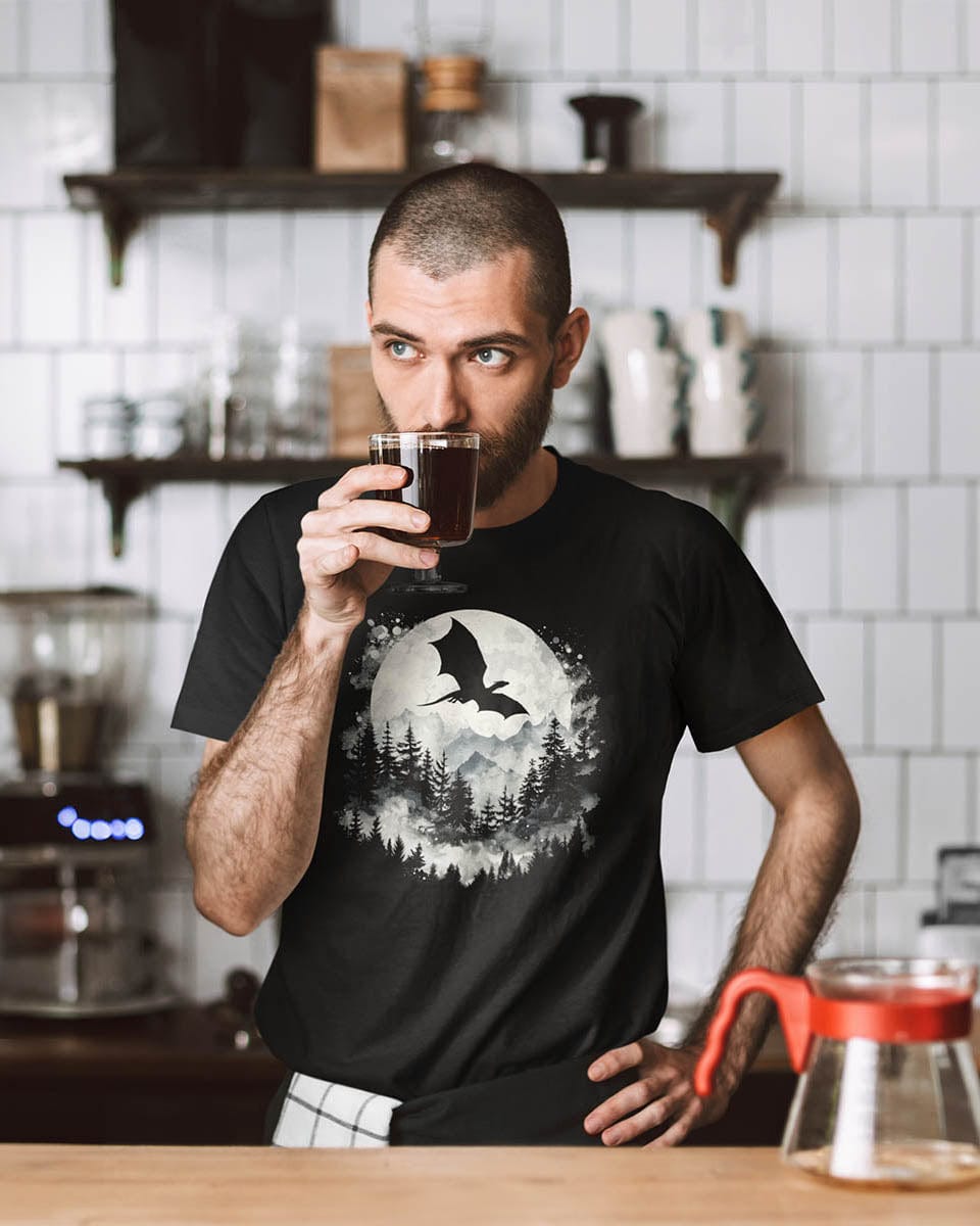 Barista with a cup of coffee wearing a Full Moon Flight Dragon shirt featuring a dragon silhouette flying past a full moon.