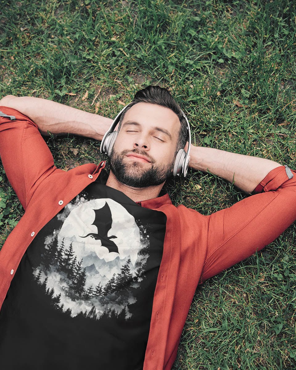 Man lying in the grass wearing a Full Moon Flight Dragon shirt featuring a flying dragon silhouette soaring past a full moon.