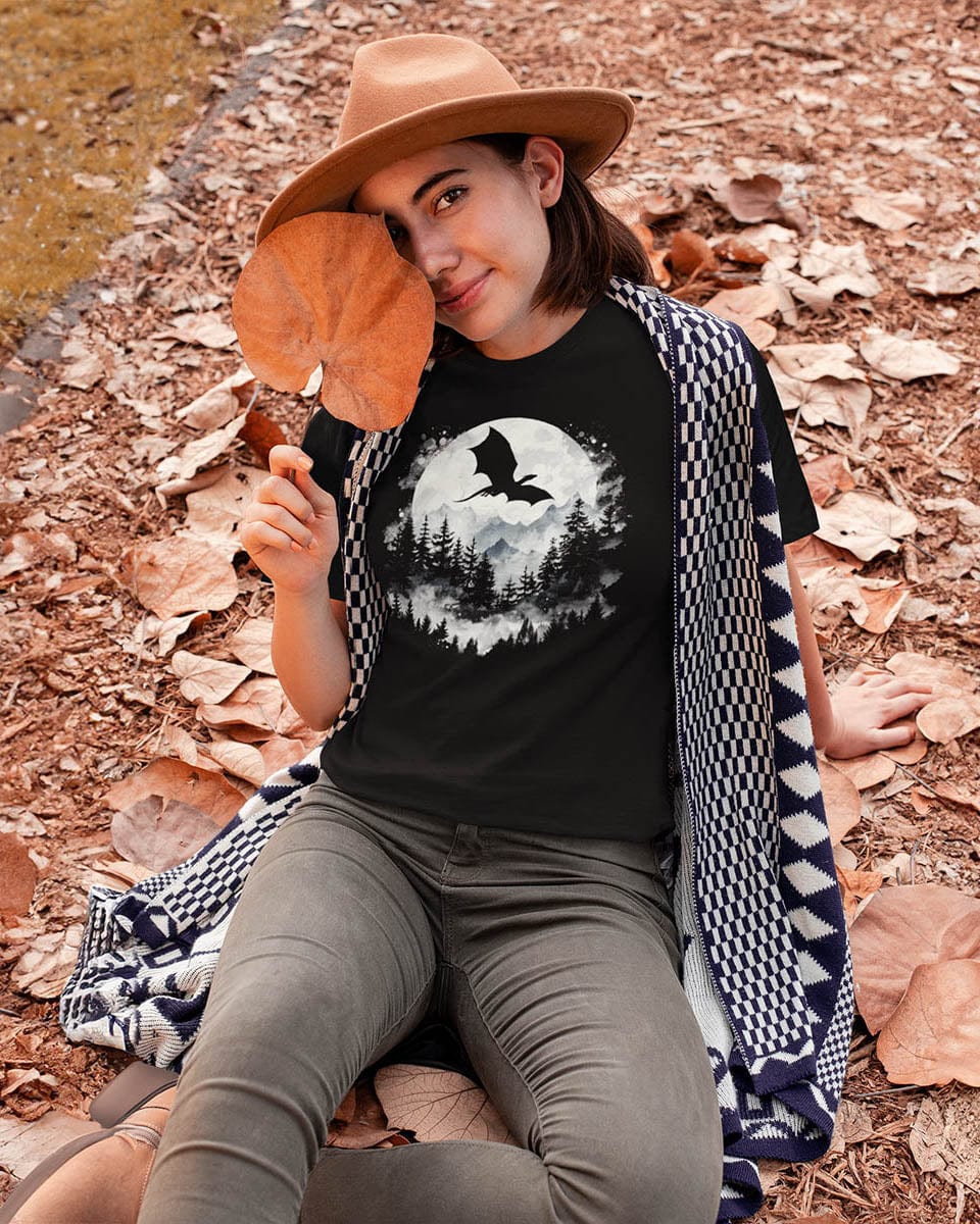 Woman sitting in fall leaves wearing a Full Moon Flight Dragon shirt featuring a dragon silhouette flying past a full moon.
