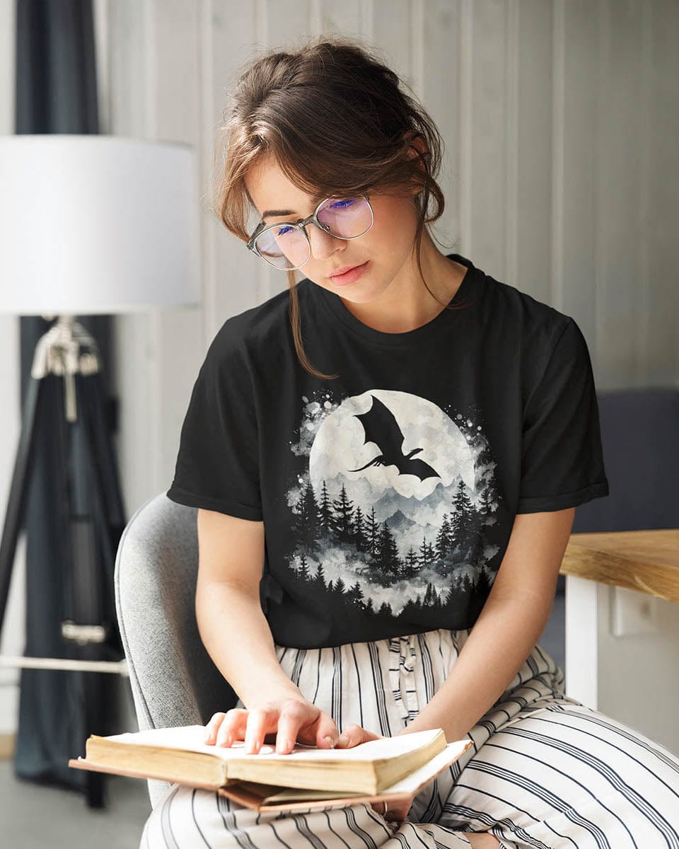 Woman reading a book wearing a Full Moon Flight Dragon shirt featuring a dragon silhouette flying past a full moon.