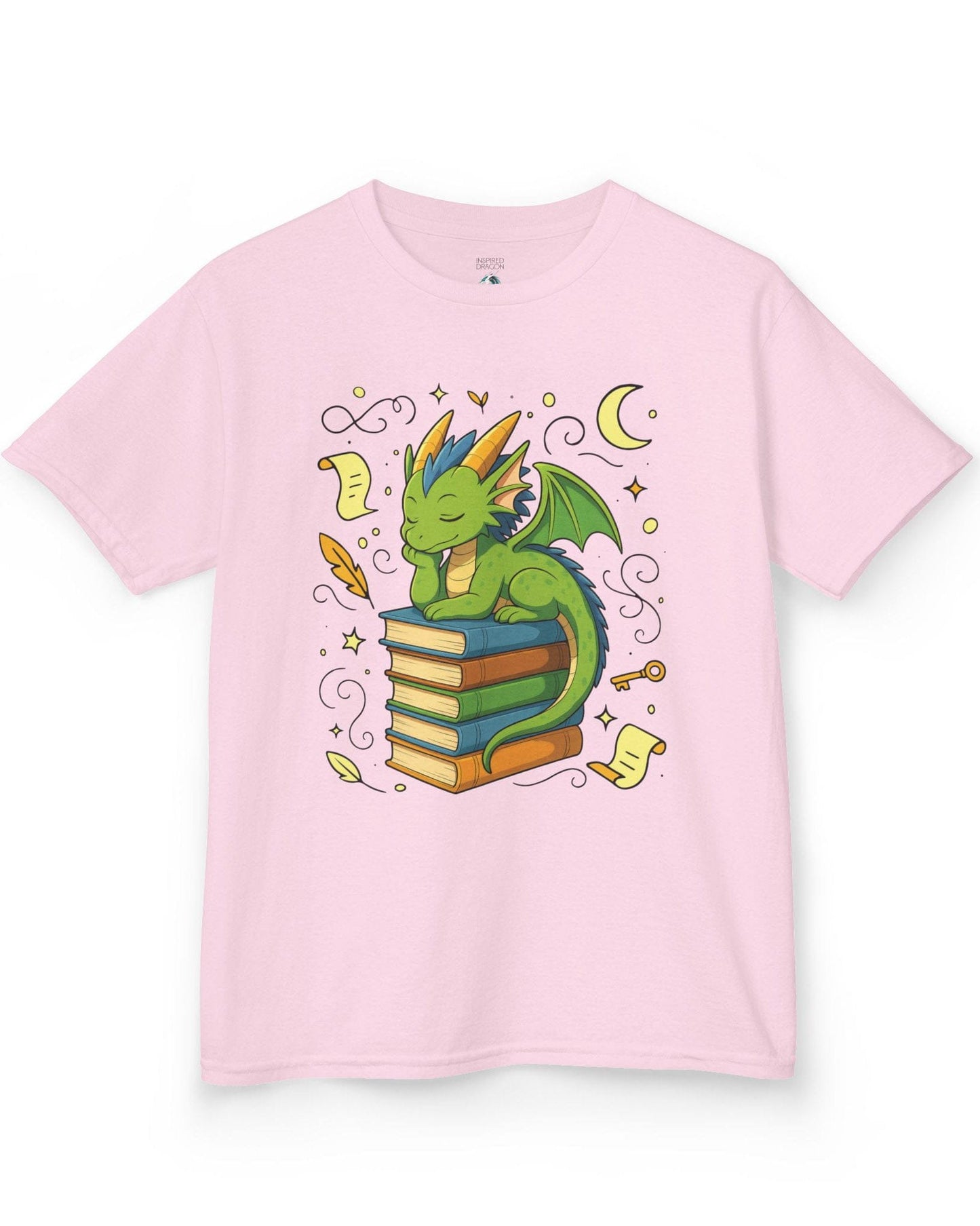 Enchanted Daydreamer shirt in light pink, featuring a sleepy green dragon resting atop a stack of colorful books.
