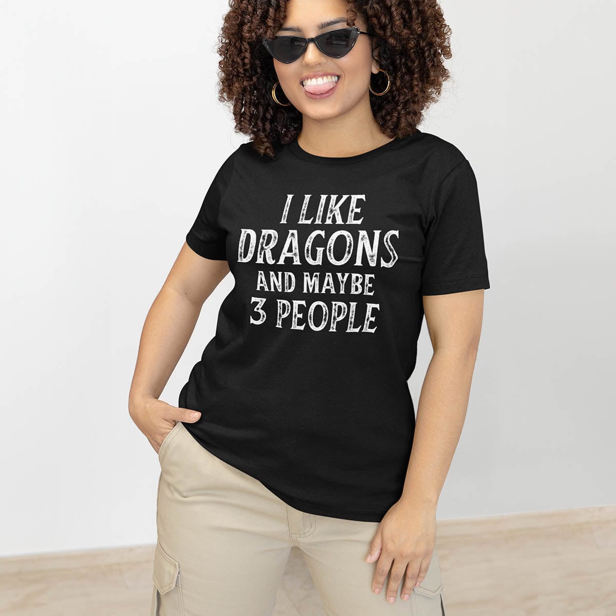 Woman wearing an I Like Dragons and Maybe 3 People Shirt with distressed text, playfully sticking out her tongue.