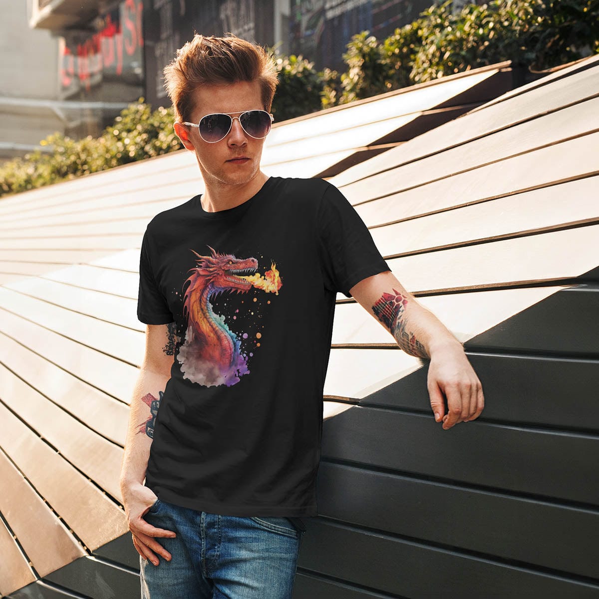 Man wearing a Fire Dragon Shirt featuring watercolor art of a fire-breathing dragon, casually leaning on a wall outdoors.