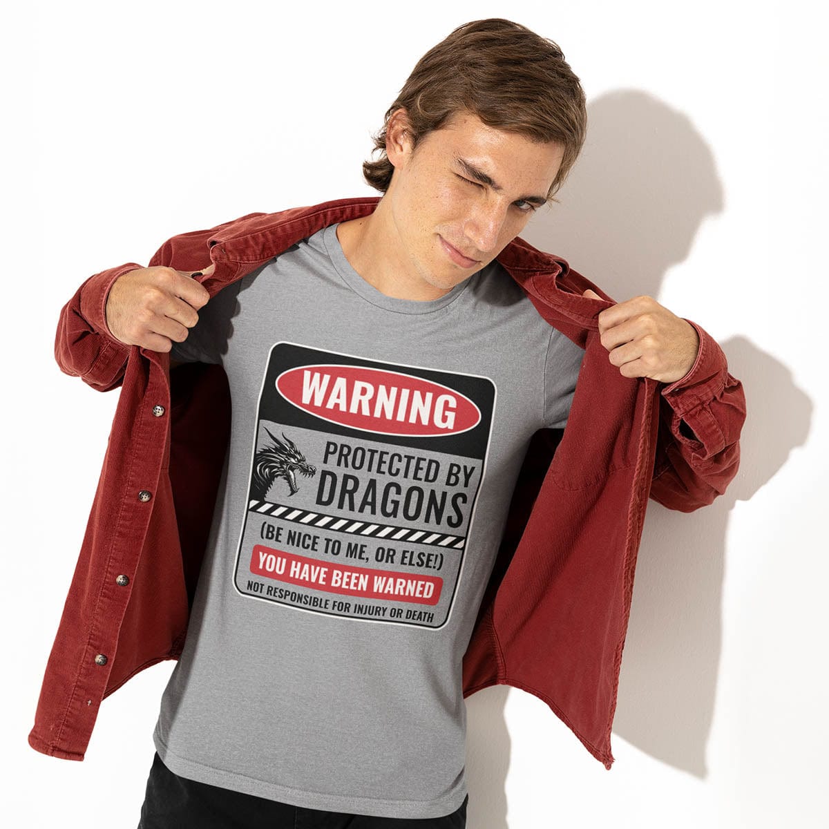 Man wearing a grey Protected by Dragons Shirt, revealing the shirt by pulling open his red jacket while winking playfully.