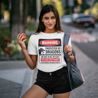 An attractive female student with an apple wearing a Protected by Dragons Shirt, smiling confidently on a city street.